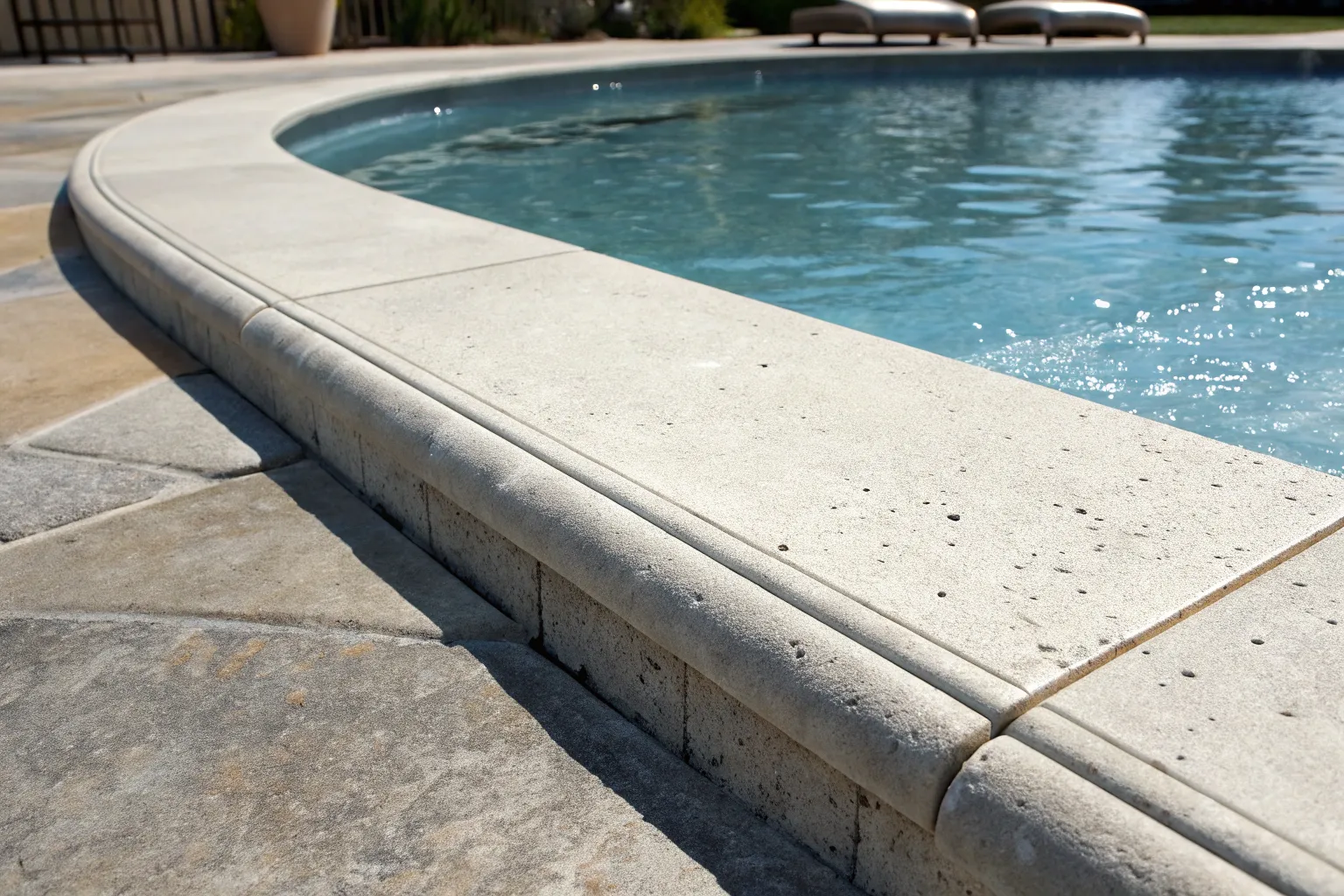 Close-up of a smooth concrete pool coping edge where the paving meets the water
